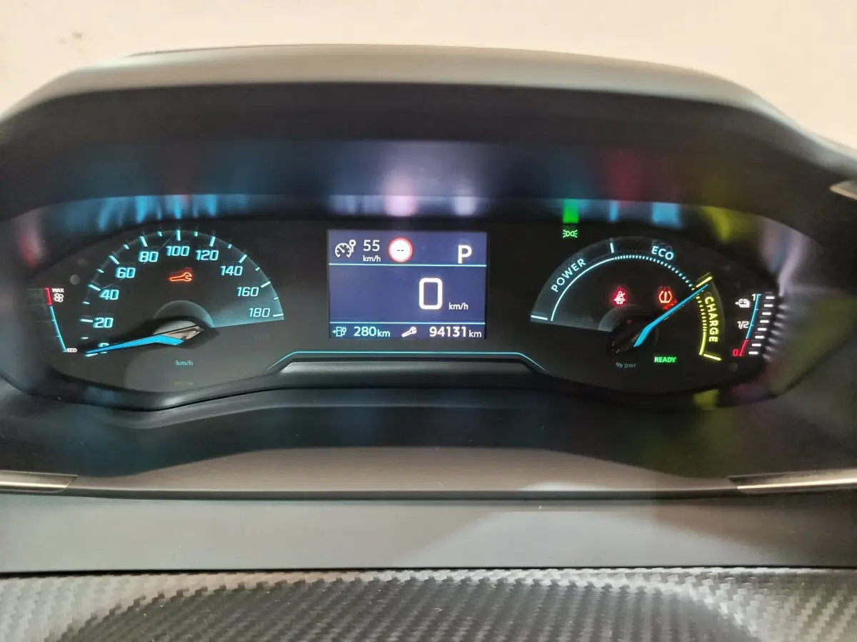 Tableau de bord numérique de Peugeot 208 électrique blanc, affichage vitesse et autonomie, vue frontale rapprochée.