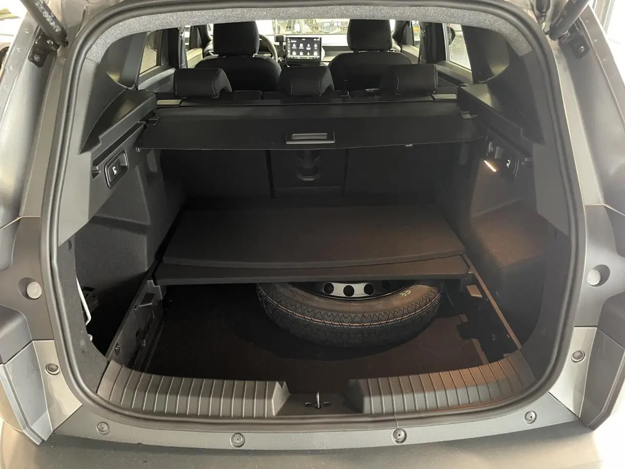 Coffre ouvert du Dacia Bigster gris schiste montrant la roue de secours galette et la banquette arrière rabattable.