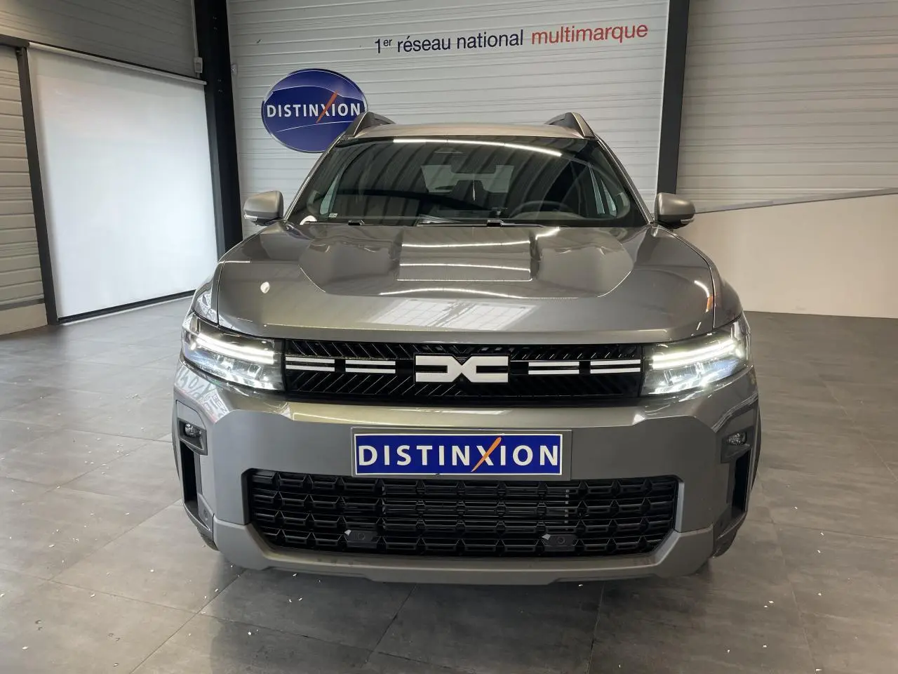 Vue avant du Dacia Bigster gris schiste avec calandre noire et signature lumineuse LED allumée en intérieur showroom.