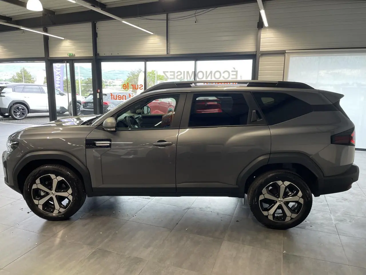 Vue de profil côté gauche du Dacia Bigster gris schiste avec jantes alliage 18 pouces diamantées en showroom.