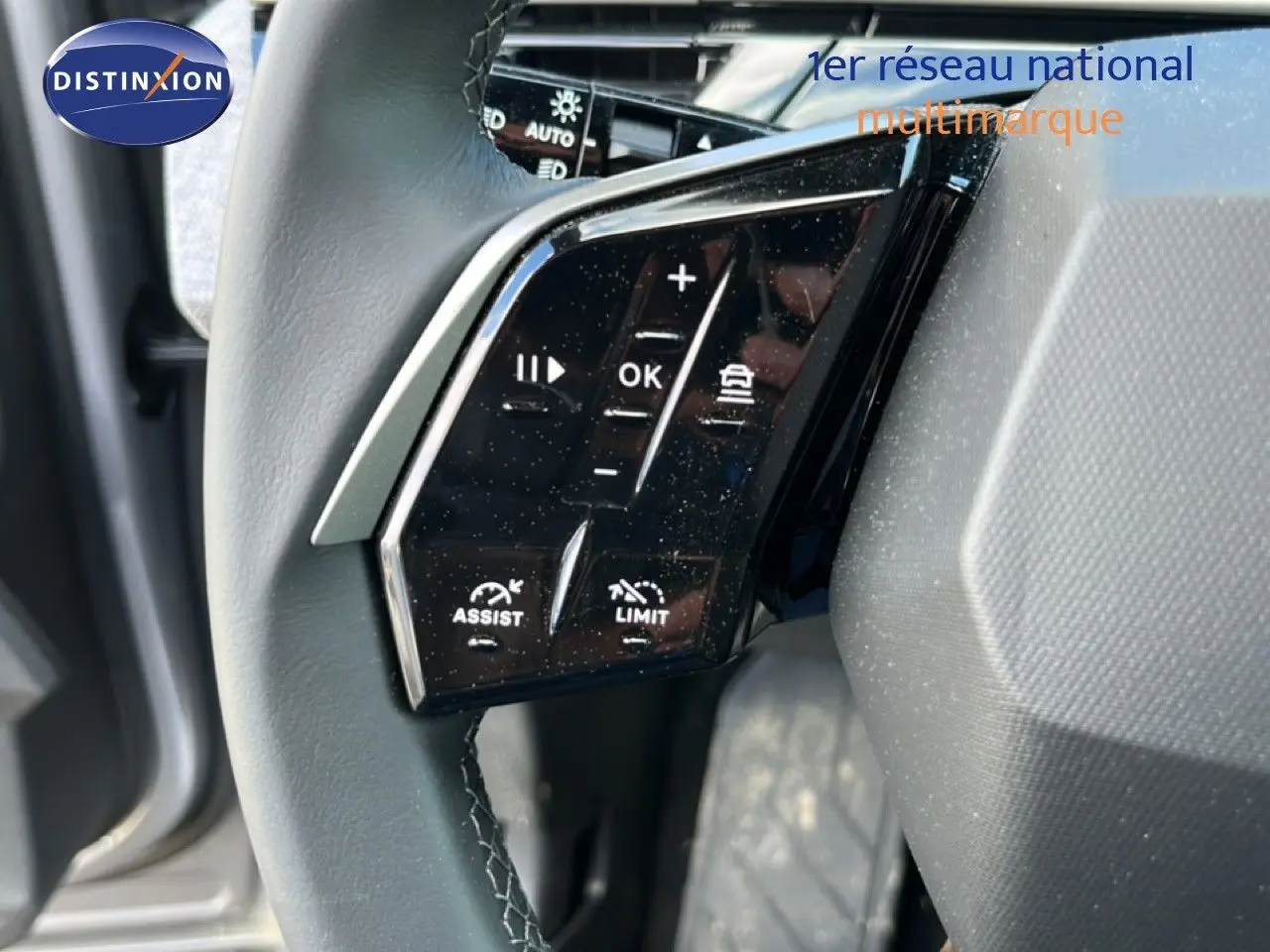 Gros plan sur les commandes du volant noir du Peugeot 5008 gris Artense, mettant en valeur les fonctions d'assistance et limiteur.