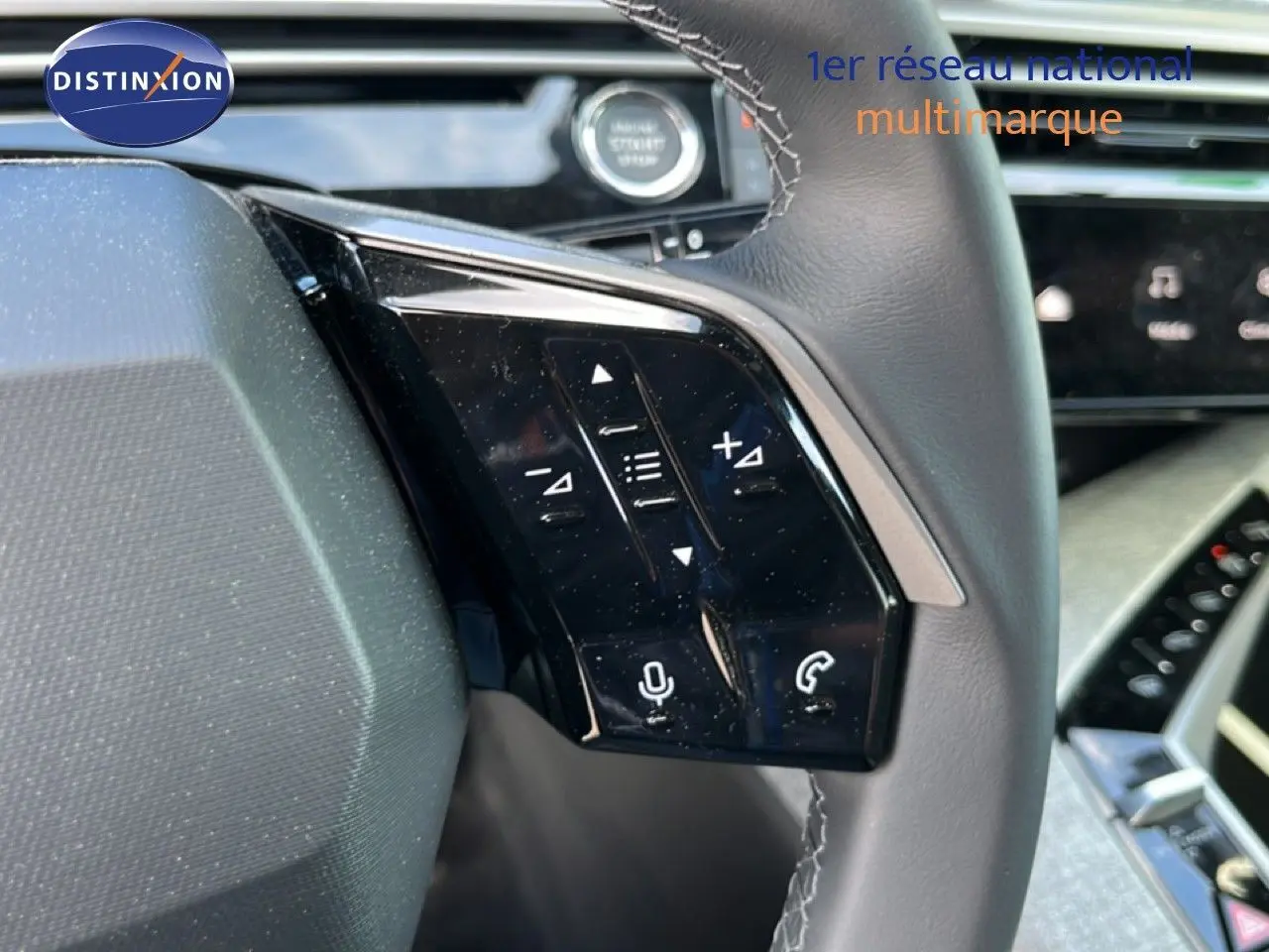 Gros plan sur les commandes gauche du volant gris cuir du Peugeot 5008 Hybrid 145ch 2025 avec tableau de bord moderne en arrière-plan.