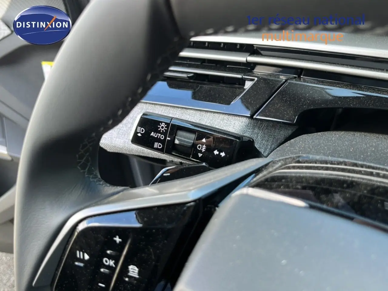 Gros plan sur le volant noir et la commande des phares du Peugeot 5008 gris Artense, intérieur moderne et soigné.
