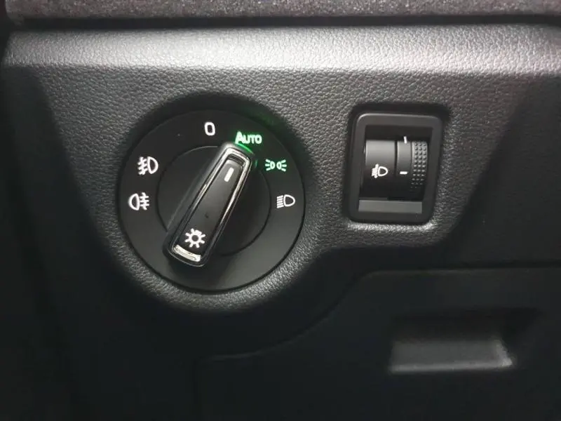 Gros plan sur le bouton de commande des phares avec réglage automatique, intérieur noir du Skoda Kamiq gris.