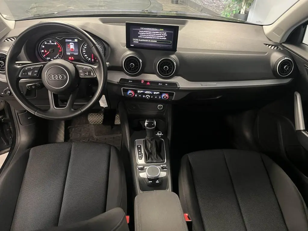 Intérieur Audi Q2 2022 vu de face, tableau de bord noir avec écran central et volant multifonction cuir.