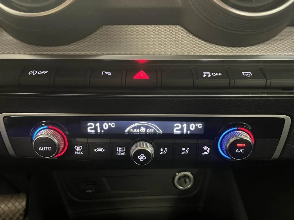 Vue rapprochée de la console centrale de l'Audi Q2 2022, affichant la climatisation automatique à 21°C avec commandes rétroéclairées.