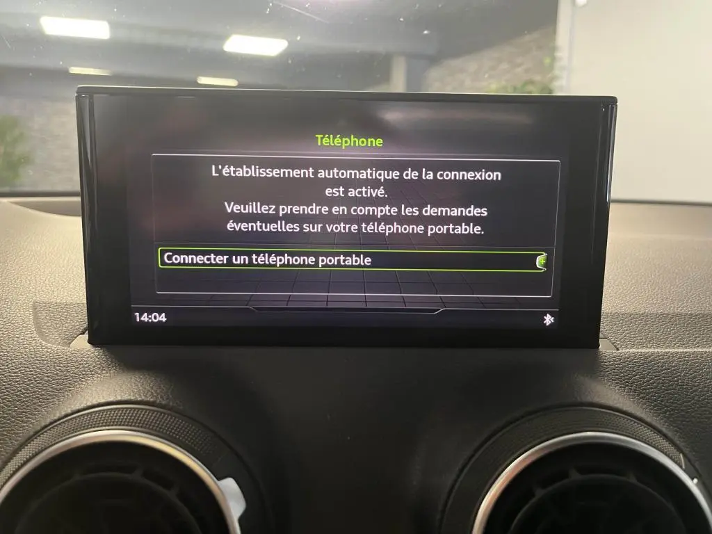 Écran central de l'Audi Q2 2022 affichant la connexion Bluetooth pour téléphone portable, entouré de grilles d'aération rondes noires.