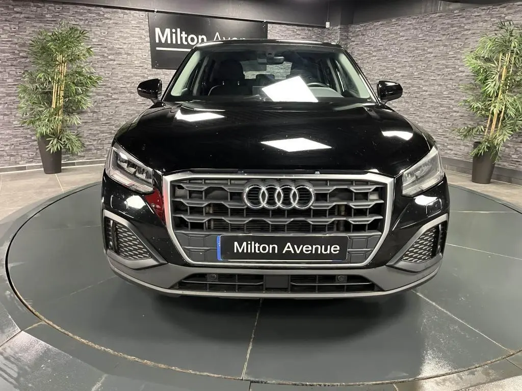 Vue frontale d'un Audi Q2 noir brillant avec calandre hexagonale et logo anneaux, en showroom intérieur.