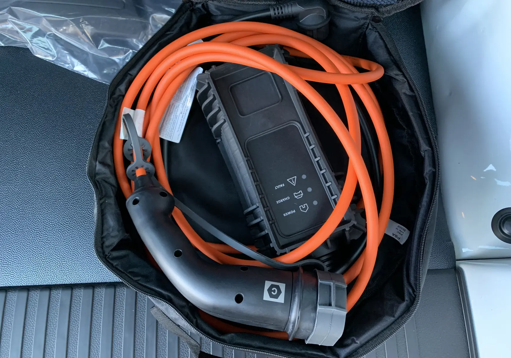 Câble de recharge électrique orange enroulé dans un sac noir, posé sur le coffre d'un FIAT Scudo Combi blanc.