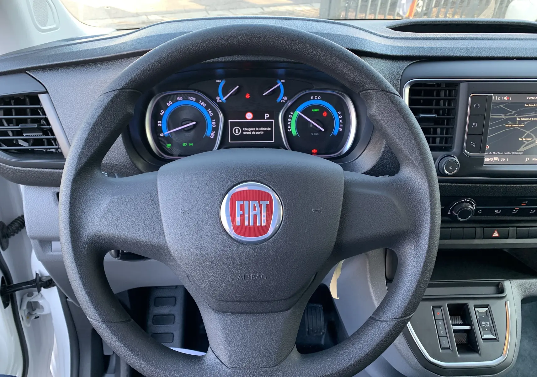 Vue centrée sur le volant noir avec logo FIAT, tableau de bord digital et console centrale d'un FIAT Scudo Combi blanc électrique 2022.