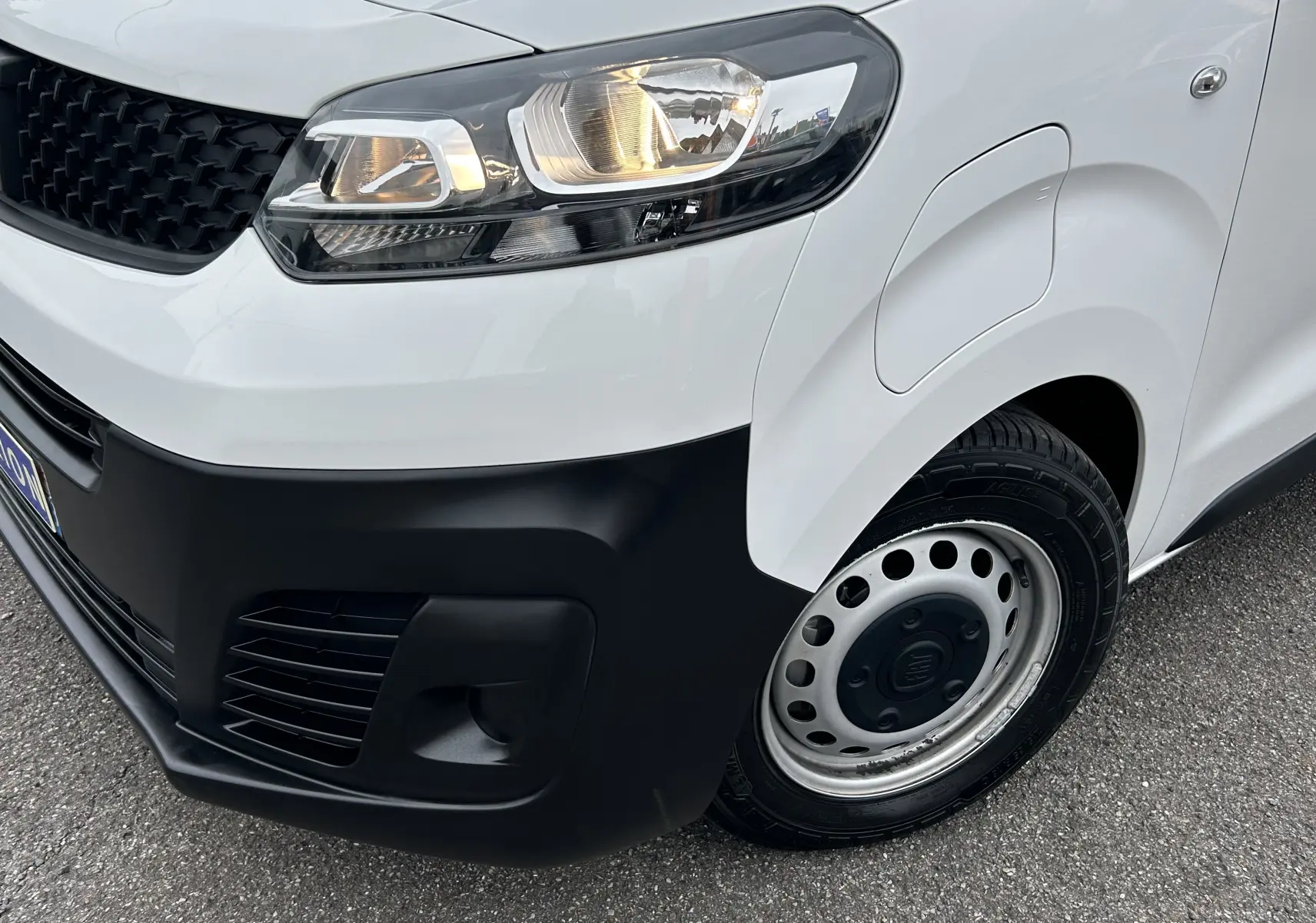 Gros plan sur l'avant droit blanc du Fiat Scudo Combi électrique 2022 avec phare allumé et jante acier simple.