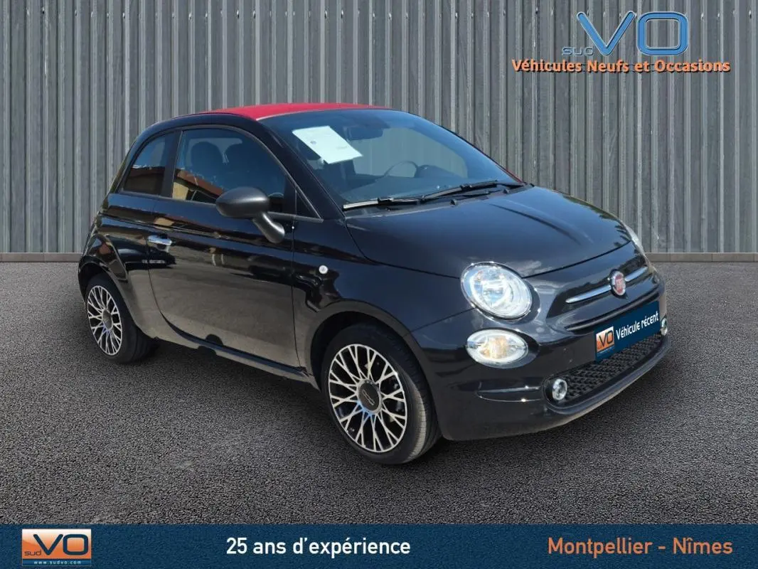 Vue 3/4 avant d'une FIAT 500C noire avec toit rouge et jantes alliage stylées, stationnée sur sol bitumé.