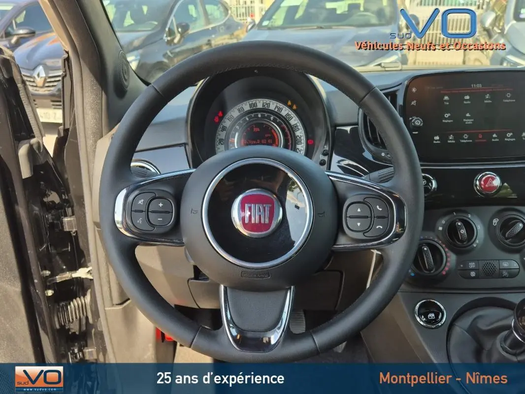 Vue intérieure centrée sur le volant de la Fiat 500C noire 2024, avec tableau de bord et commandes visibles.