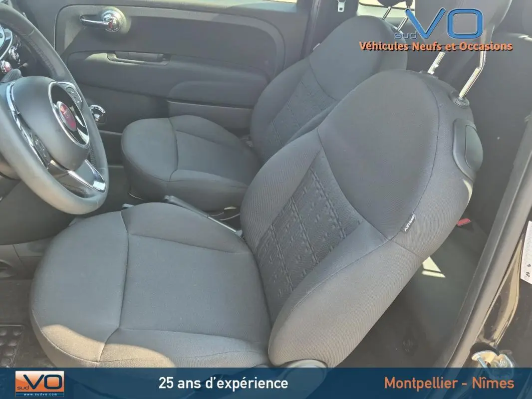 Intérieur avant du Fiat 500C noir 2024, montrant les sièges tissu gris et le volant côté gauche.