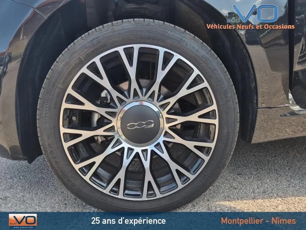 Gros plan sur la roue avant droite d'une FIAT 500C noire 2024 avec jante alliage au design étoilé.