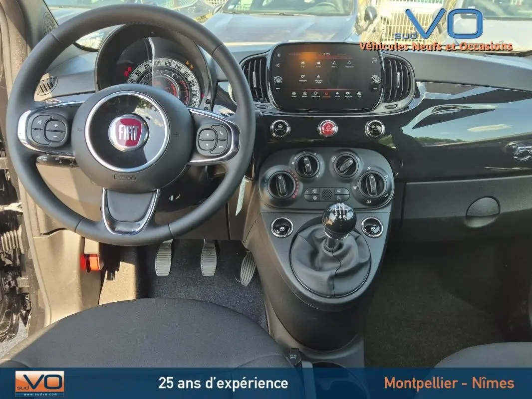Intérieur avant de la FIAT 500C noire 2024, volant, tableau de bord et levier de vitesses manuel visibles.