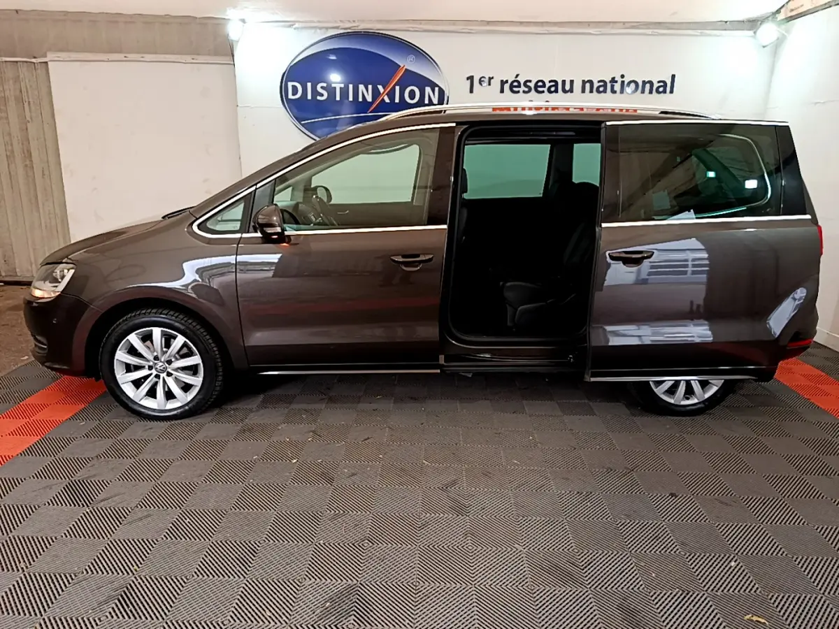 Vue latérale gauche d'un Volkswagen Sharan marron 2017 avec porte coulissante arrière ouverte en intérieur showroom.