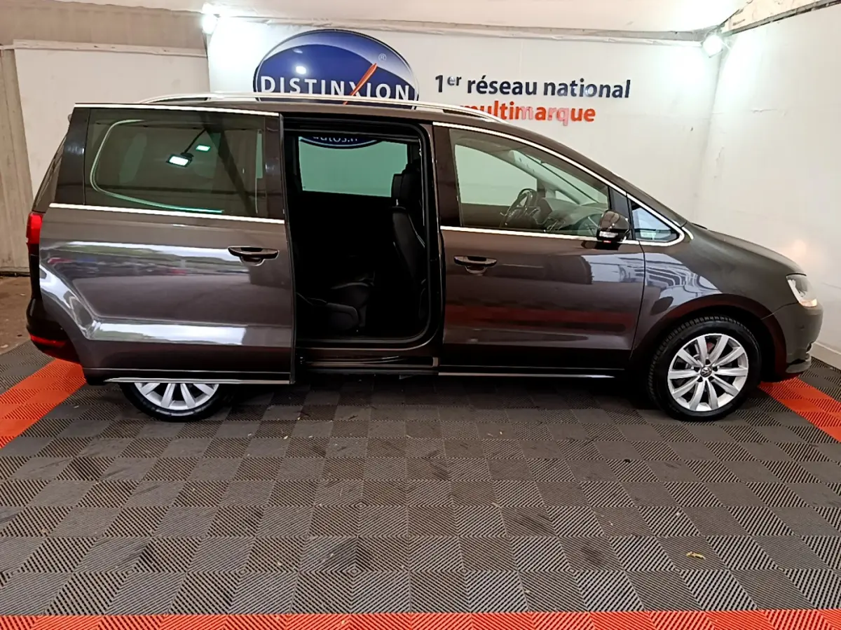 Profil droit d'un Volkswagen Sharan marron 2017 avec porte coulissante arrière ouverte en intérieur showroom.