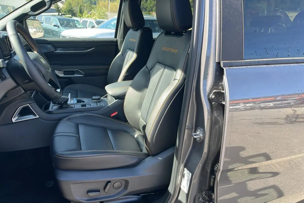 Vue intérieure côté conducteur du Ford Ranger gris carbone 2025, sièges cuir noirs avec surpiqûres orange et logo Wildtrak brodé.