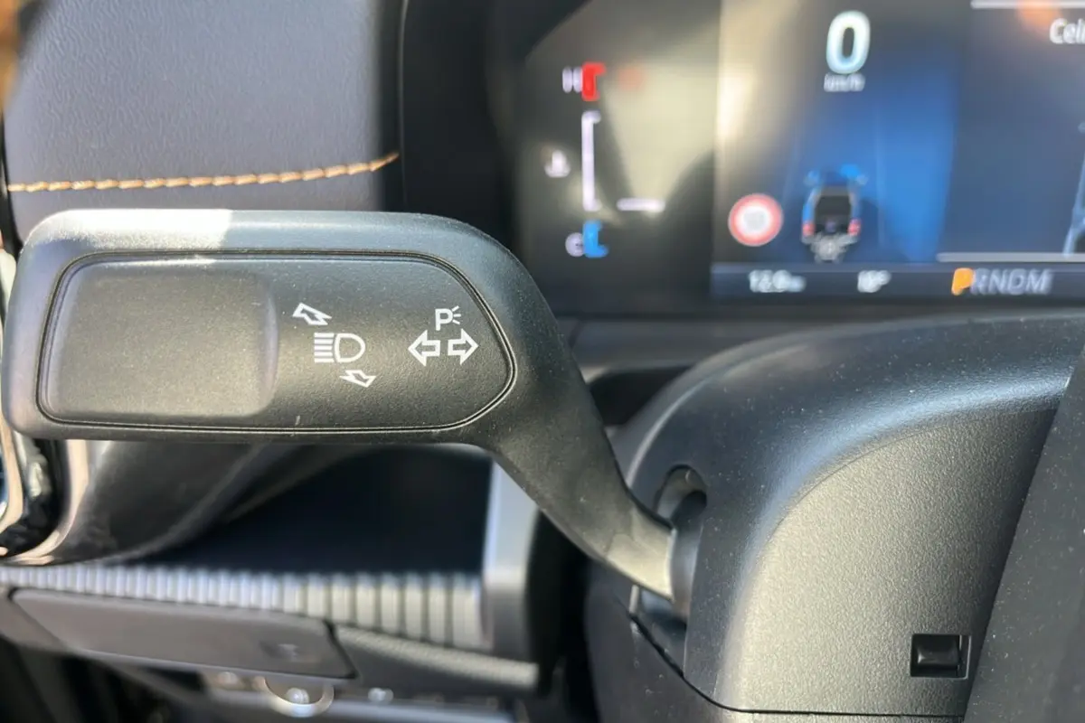 Gros plan sur la manette de clignotant à gauche du volant du Ford Ranger gris carbone, tableau de bord numérique en arrière-plan.