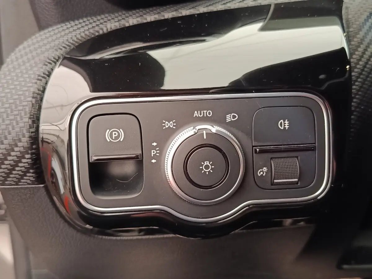 Gros plan sur la commande des phares et frein à main électrique dans l’habitacle noir brillant de la Mercedes Classe A gris clair.
