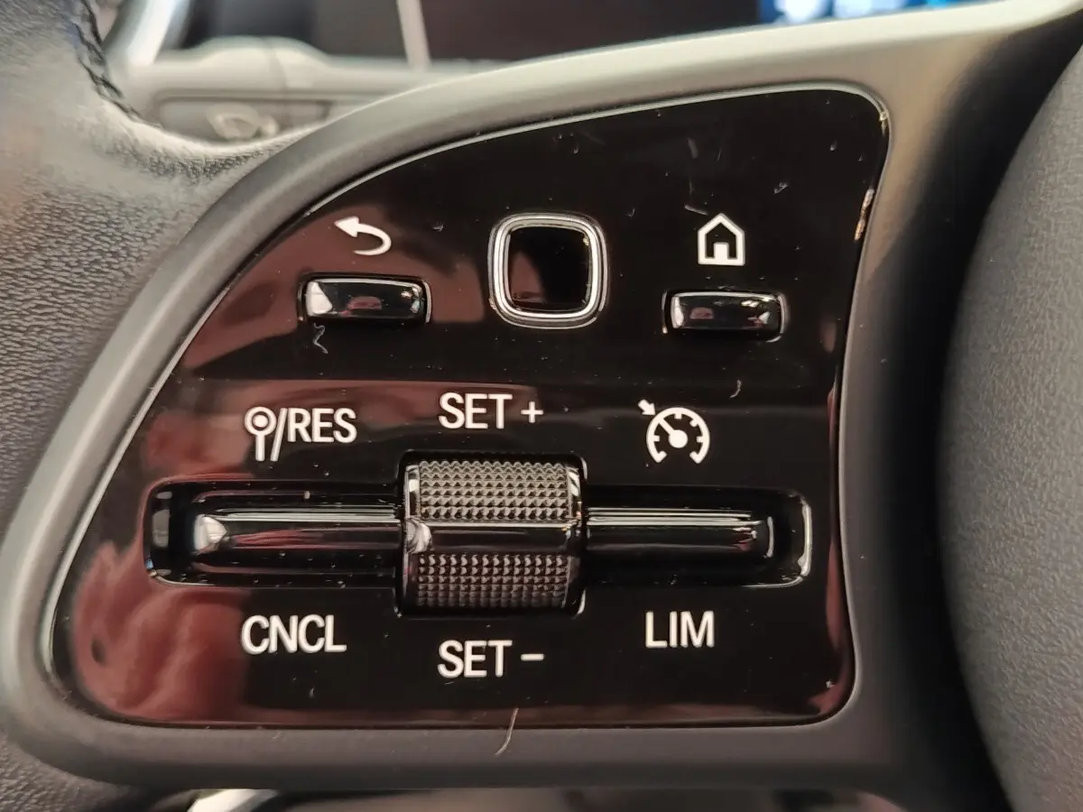 Gros plan sur les commandes de régulateur de vitesse au volant cuir noir de la Mercedes Classe A gris clair.