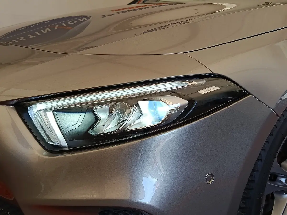 Gros plan sur le phare avant droit d’une Mercedes Classe A 180 Business Line gris clair, avec capteur de stationnement visible.