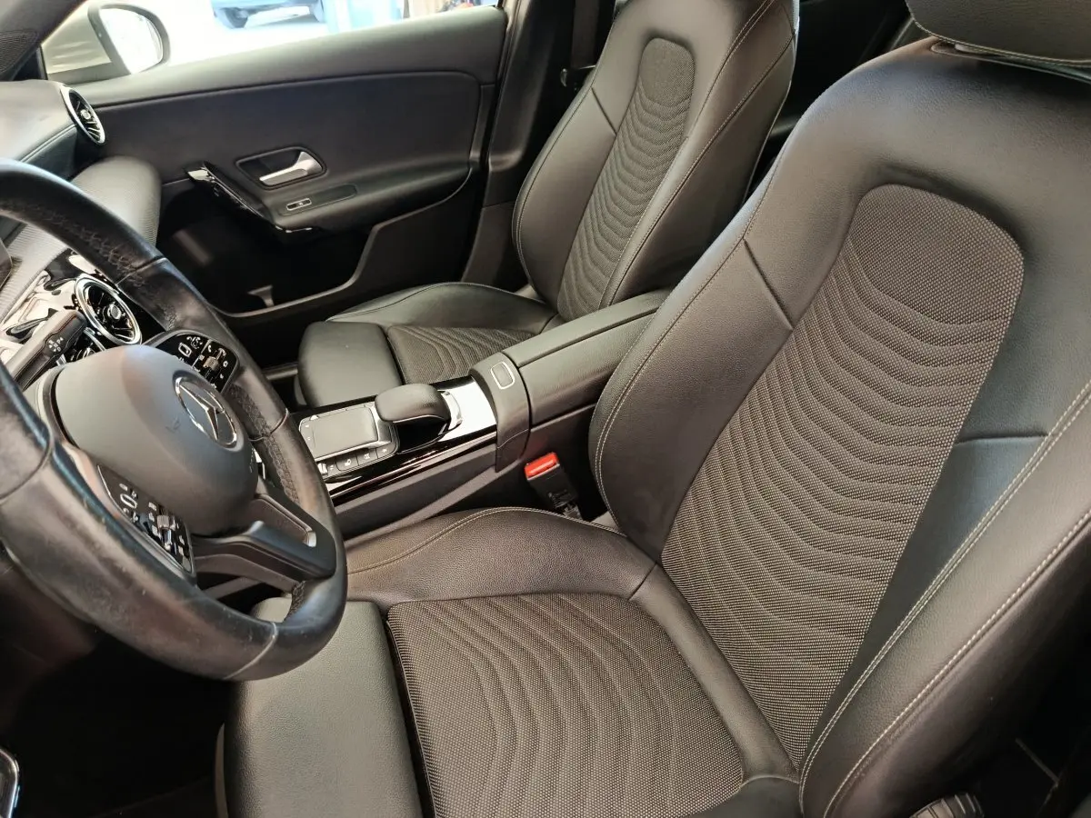 Vue intérieure côté conducteur de la Mercedes Classe A 180 Business Line 2020 avec sièges cuir noirs et volant multifonctions.
