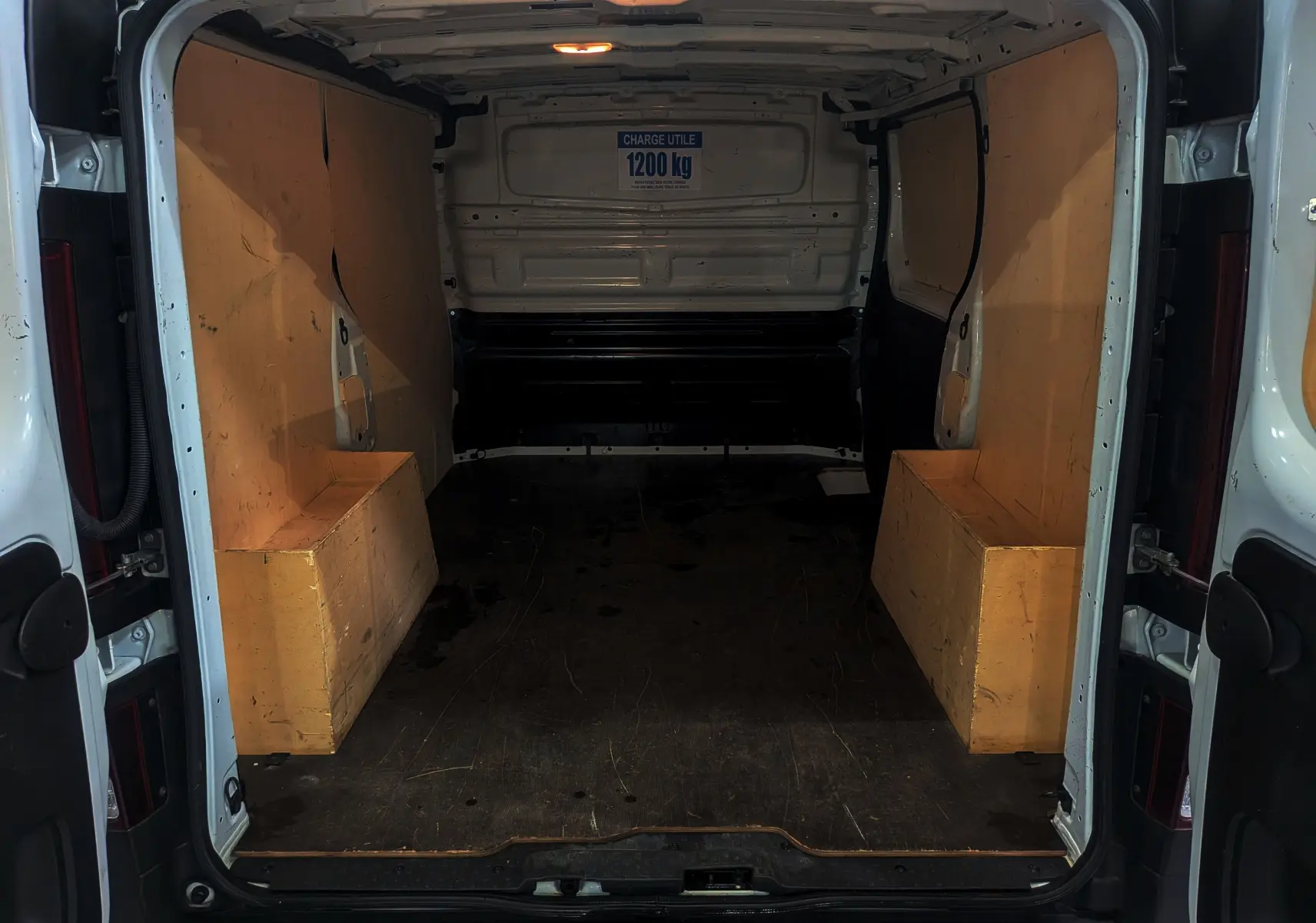 Intérieur du Renault Trafic Fourgon blanc minéral 2024, vue arrière ouverte montrant l’espace de chargement avec protections latérales en bois.