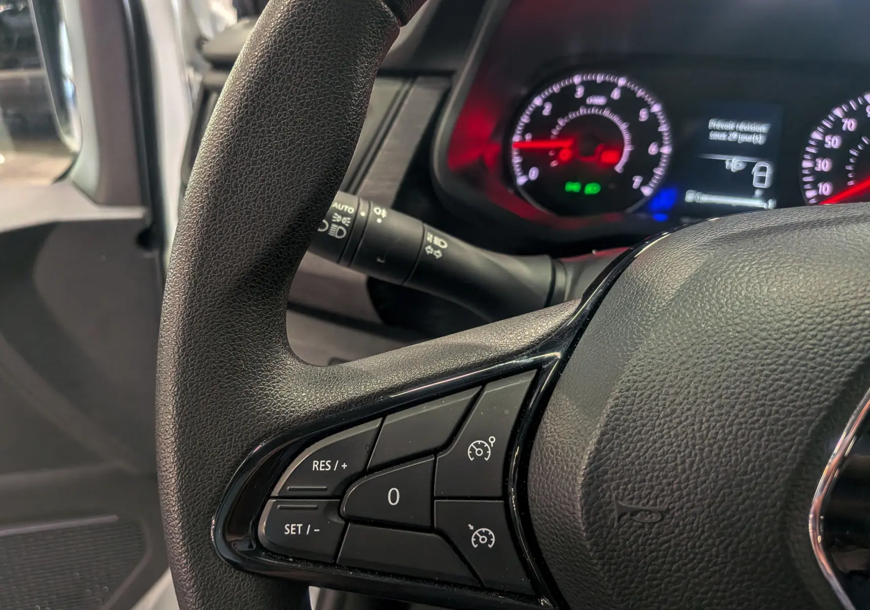 Gros plan sur le volant noir du Renault Trafic Fourgon 2024 avec commandes de régulateur de vitesse et tableau de bord lumineux.