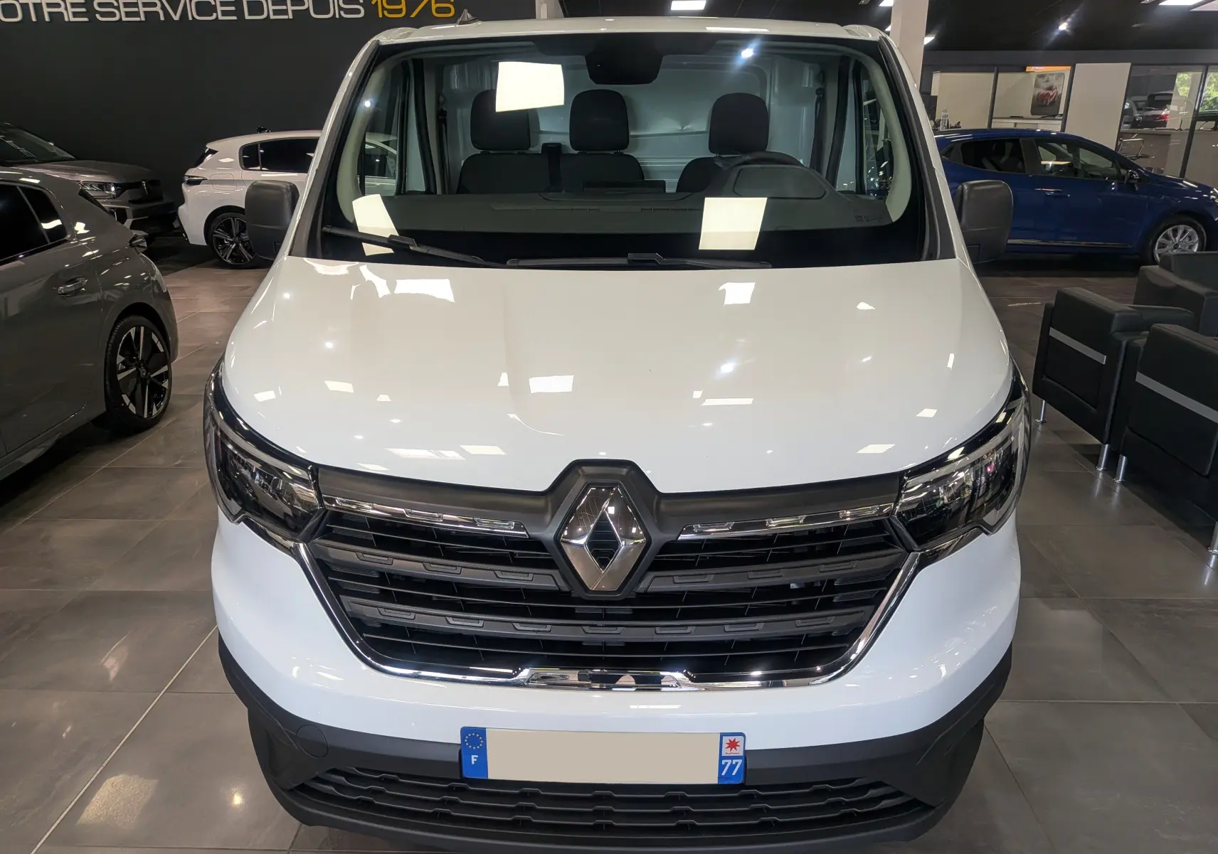 Vue frontale d'un Renault Trafic Fourgon blanc minéral 2024 avec calandre noire et logo chromé, en intérieur showroom.