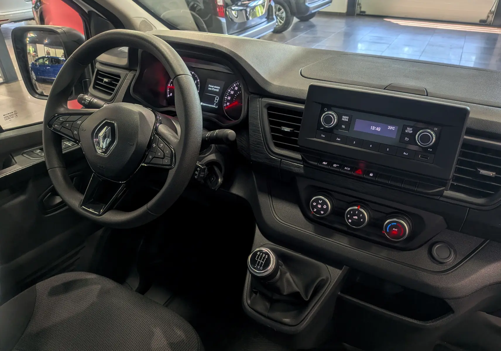 Vue intérieure côté conducteur du Renault Trafic Fourgon 2024, tableau de bord noir avec écran central et levier de vitesses manuel.