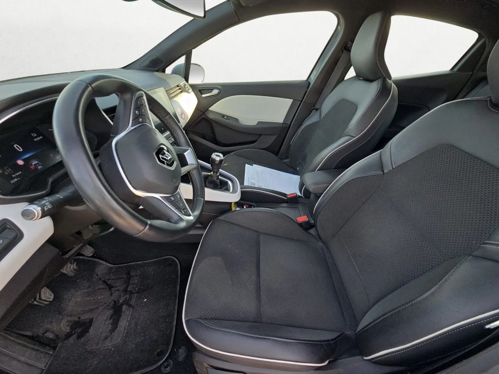 Vue intérieure côté conducteur de la Renault Clio V TCE 90 21 Intens, sièges noirs avec surpiqûres blanches et volant multifonction.