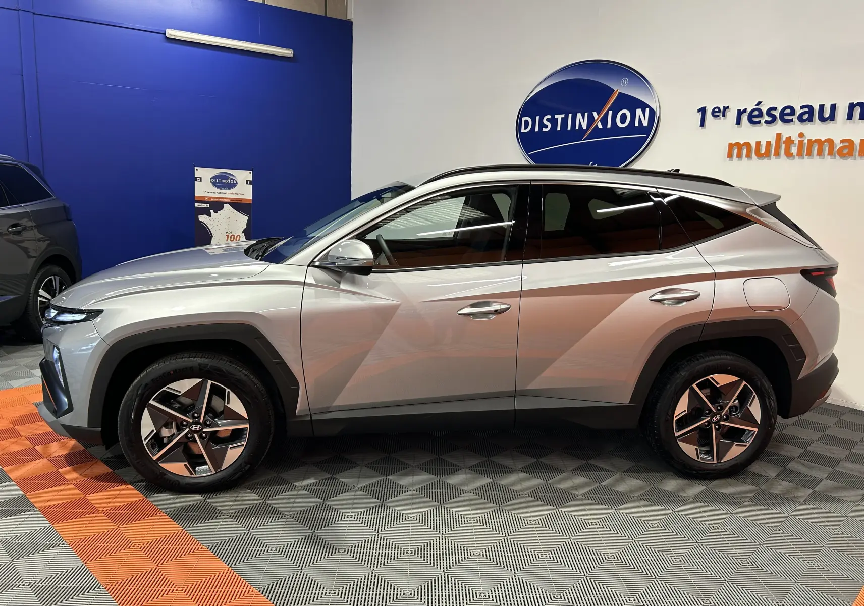 Vue de profil côté gauche du Hyundai Tucson 2025 hybride en Shimmering Silver avec jantes 18 pouces et vitres surteintées.