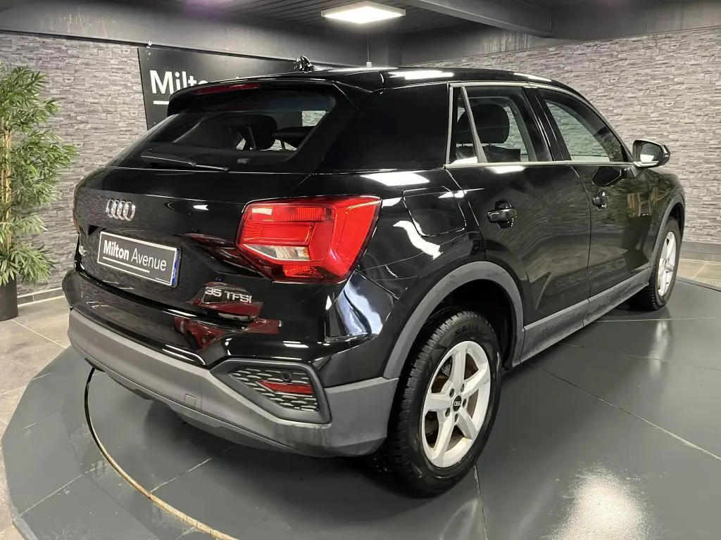 Audi Q2 noir vue 3/4 arrière droit en intérieur, avec feux arrière LED et jantes aluminium 16 pouces.