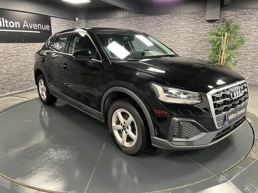 Audi Q2 noir vue 3/4 avant droit avec calandre chromée et jantes aluminium 16 pouces dans un showroom.