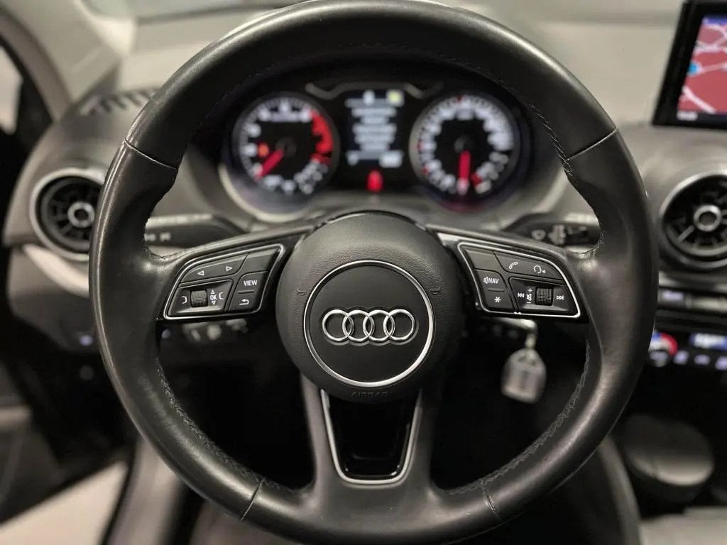Vue intérieure centrée sur le volant cuir multifonction et la console avec écran de navigation de l'Audi Q2 noire.