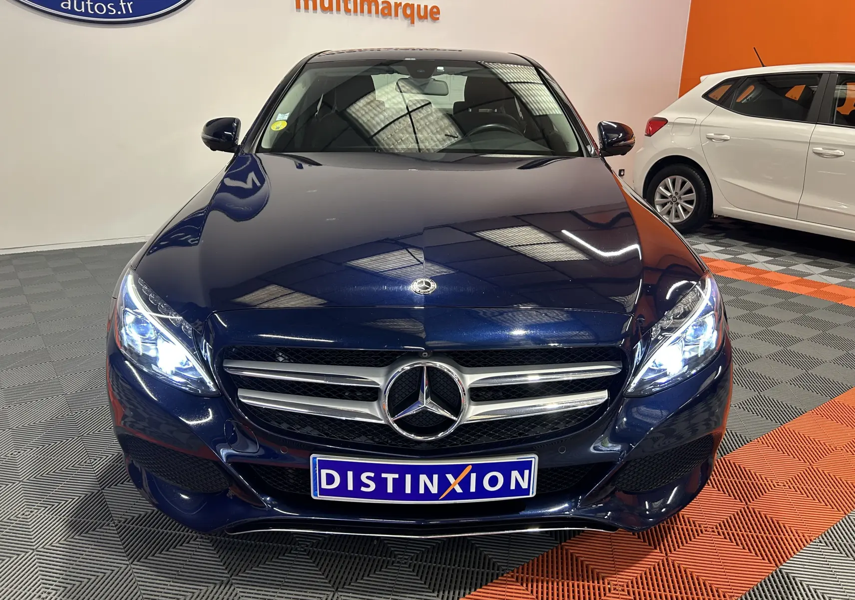 Vue frontale d'une Mercedes Classe C 200d bleu avec phares allumés et calandre chromée dans un showroom.