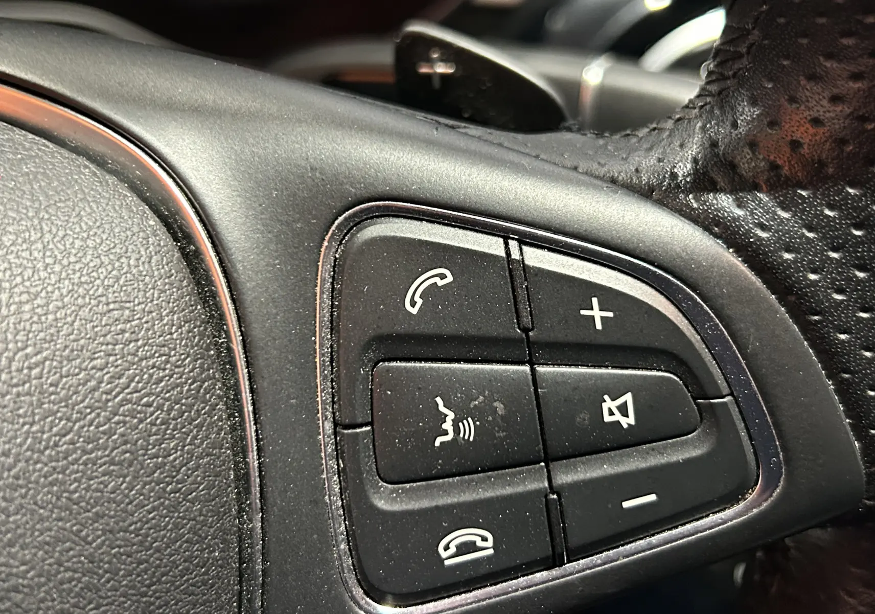 Gros plan sur les commandes audio et téléphone au volant en cuir perforé d'une Mercedes Classe C bleu 2018.