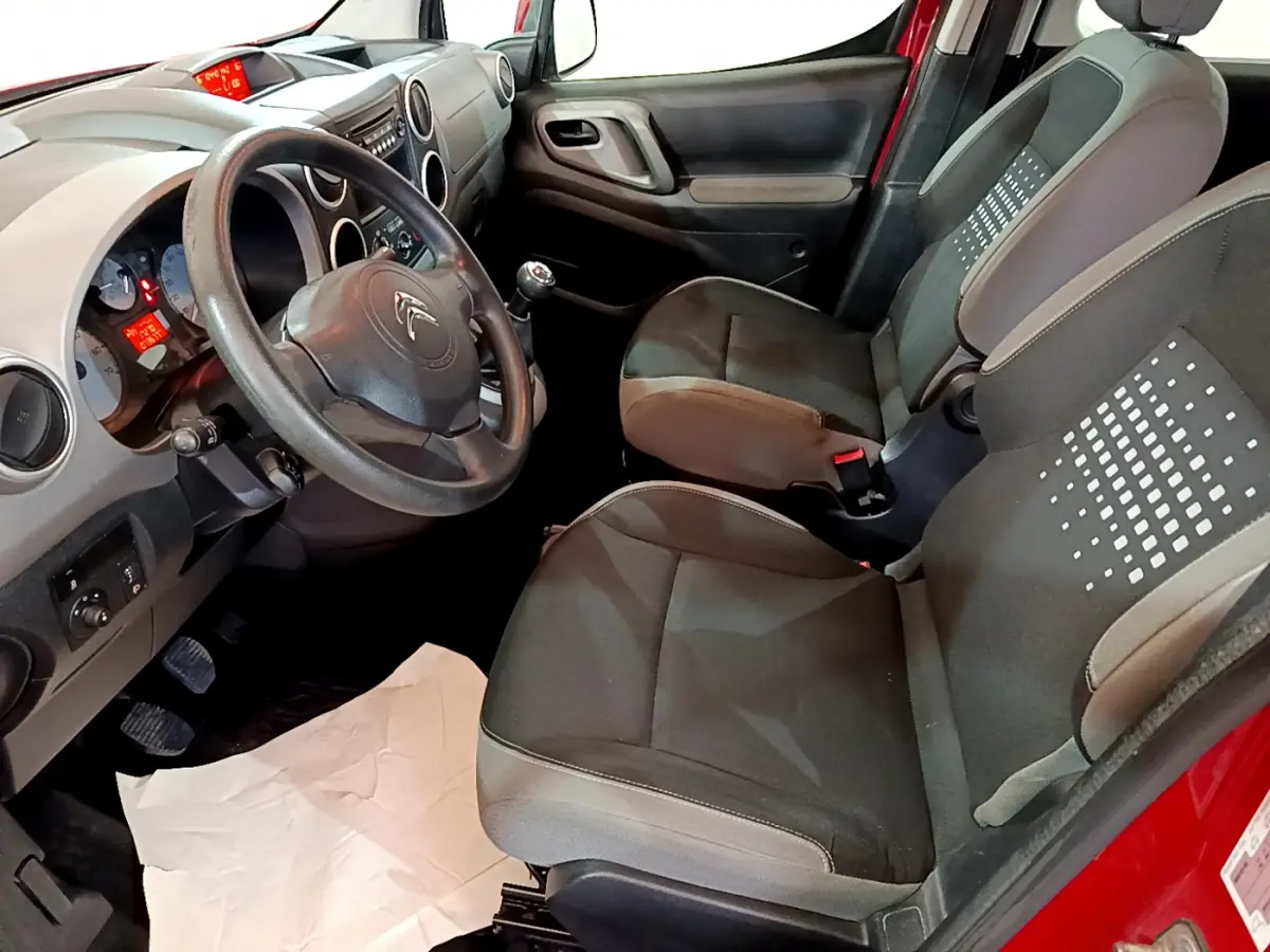 Vue intérieure côté conducteur du Citroën Berlingo rouge 2016, montrant sièges noirs et tableau de bord avec volant.