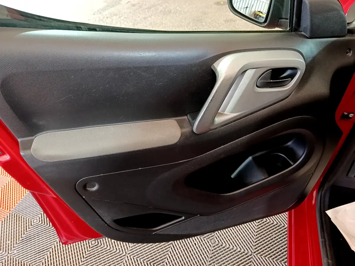 Vue rapprochée de la porte avant gauche rouge du Citroën Berlingo 2016, montrant la poignée intérieure et les rangements.