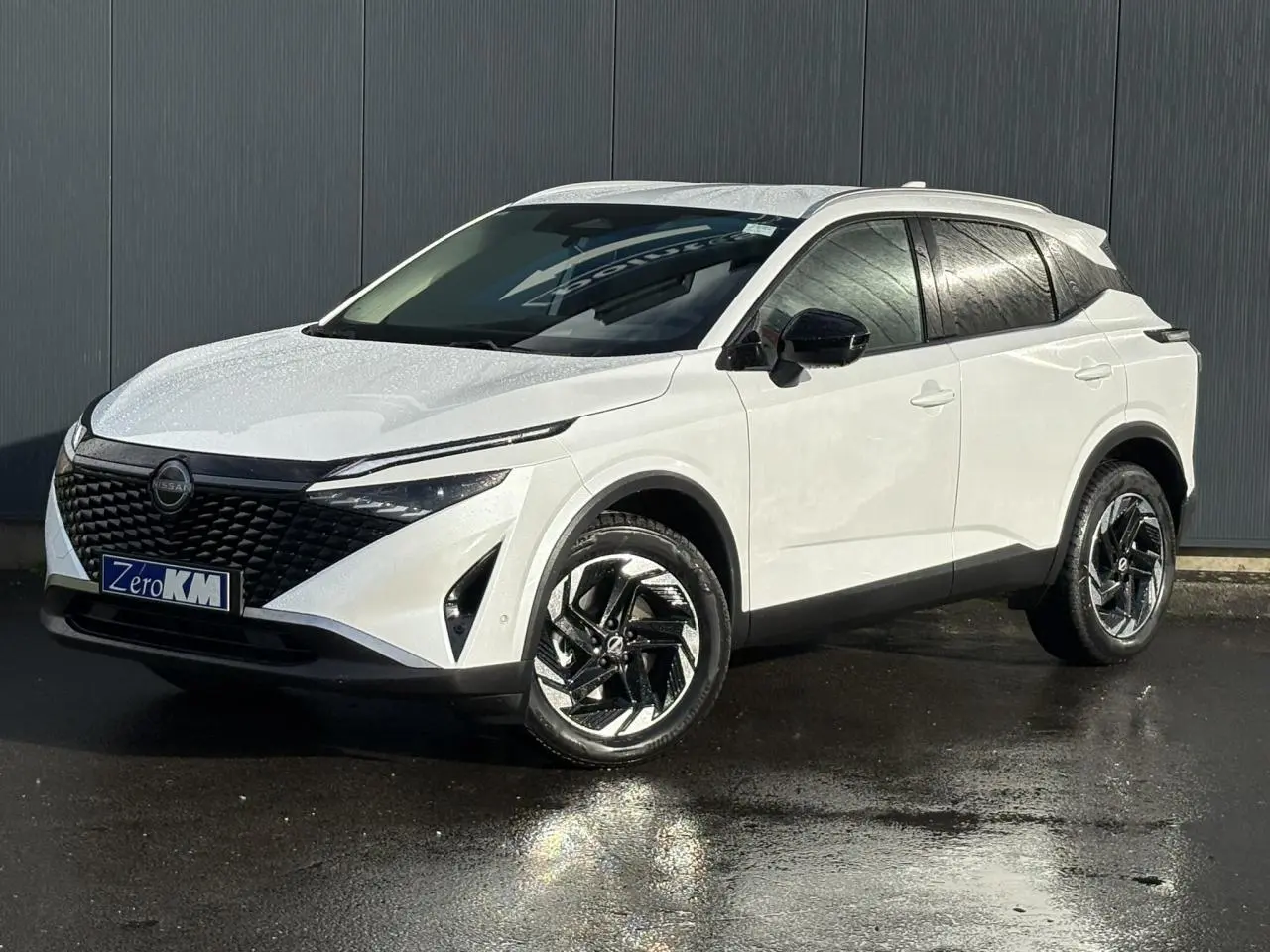 Nissan Qashqai blanc nacré en 3/4 avant droit, avec calandre noire et jantes alliage 18 pouces distinctives.