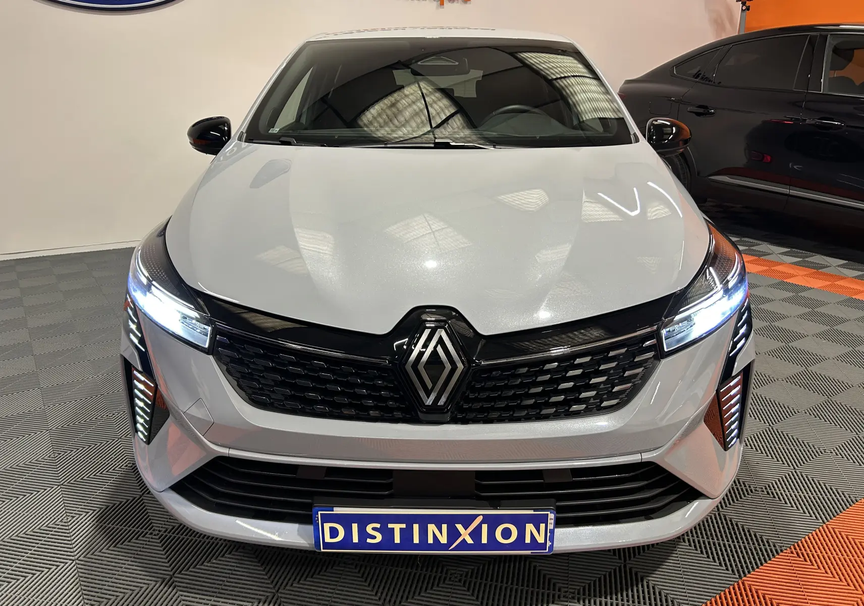 Vue avant d'une Renault Clio V E-Tech gris rafale métal avec phares LED allumés en intérieur showroom.