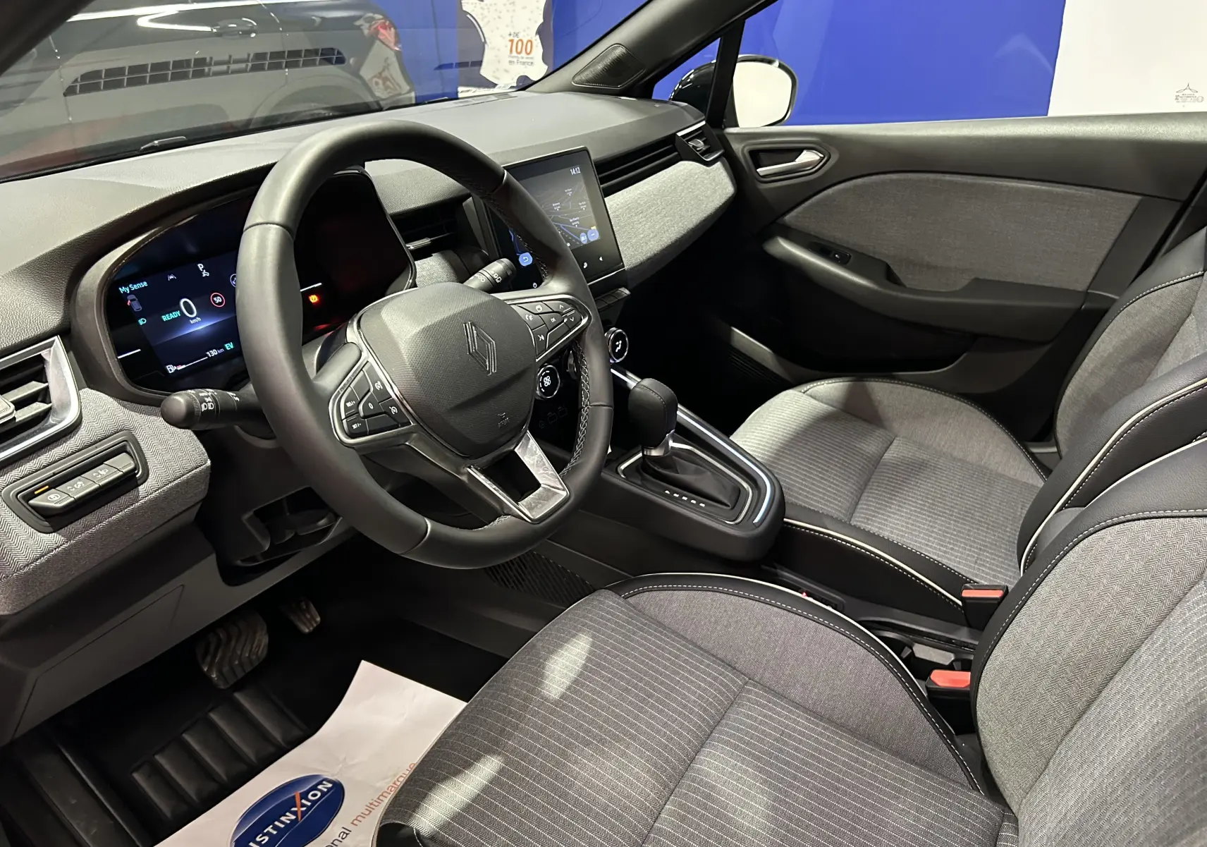 Vue intérieure côté conducteur de la Renault Clio V E-Tech 145ch gris Rafale, avec volant multifonction et écran tactile central.