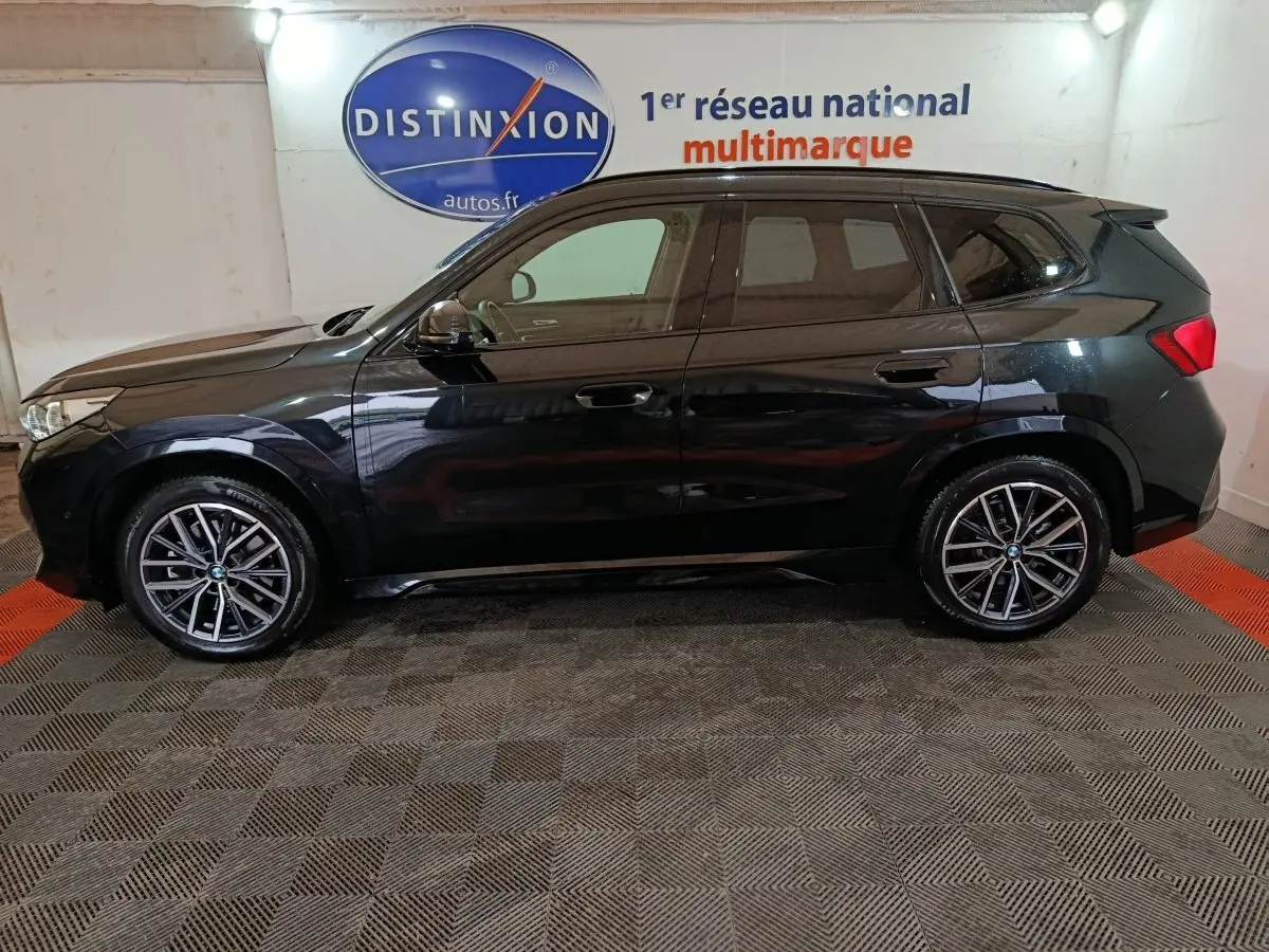 BMW X1 xDrive23i M Sport noir vue de profil côté gauche, avec jantes alliage et vitres teintées en intérieur showroom.