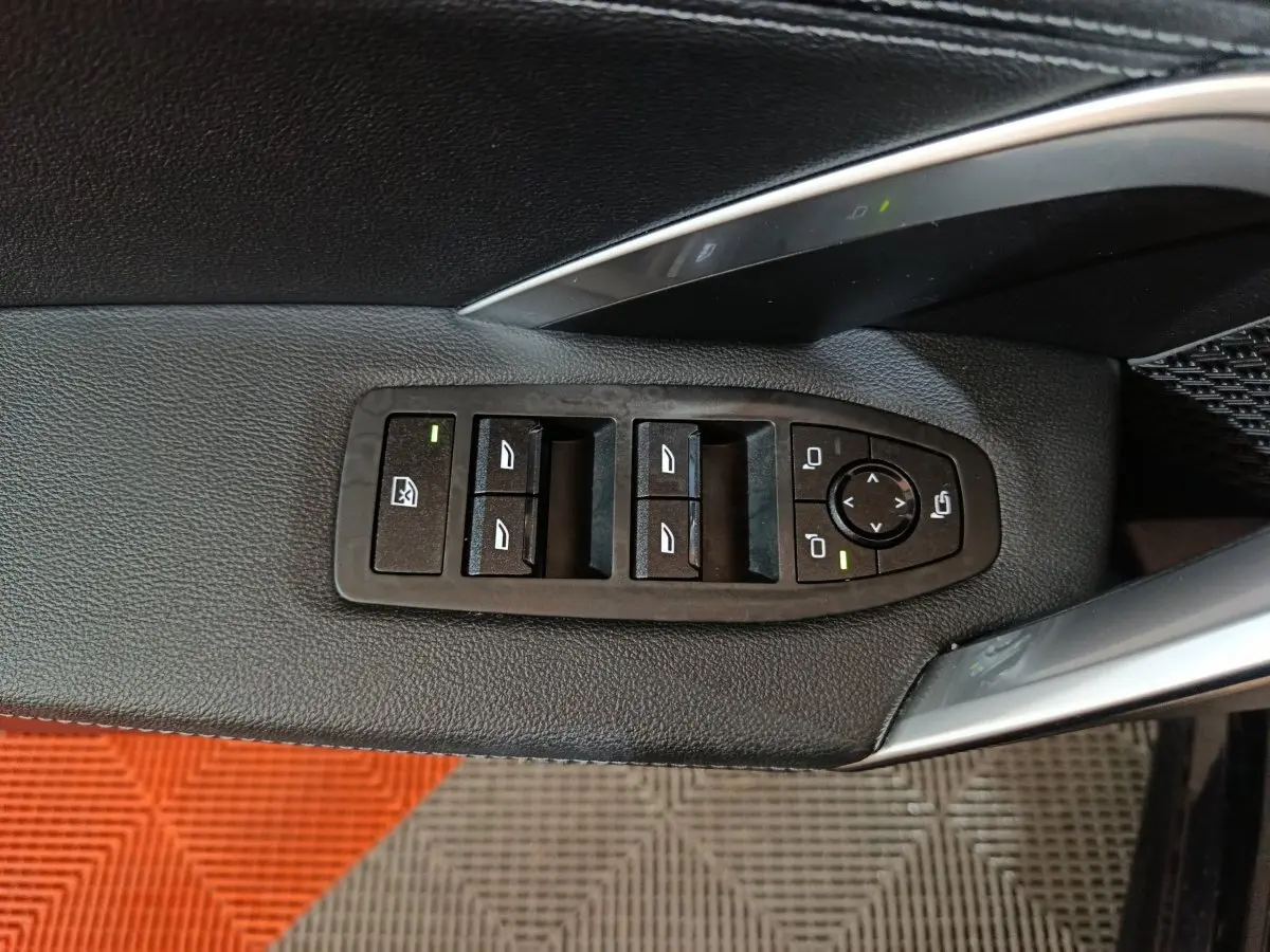 Gros plan sur les commandes de lève-vitres et rétroviseurs côté conducteur d’un BMW X1 noir, intérieur cuir noir.