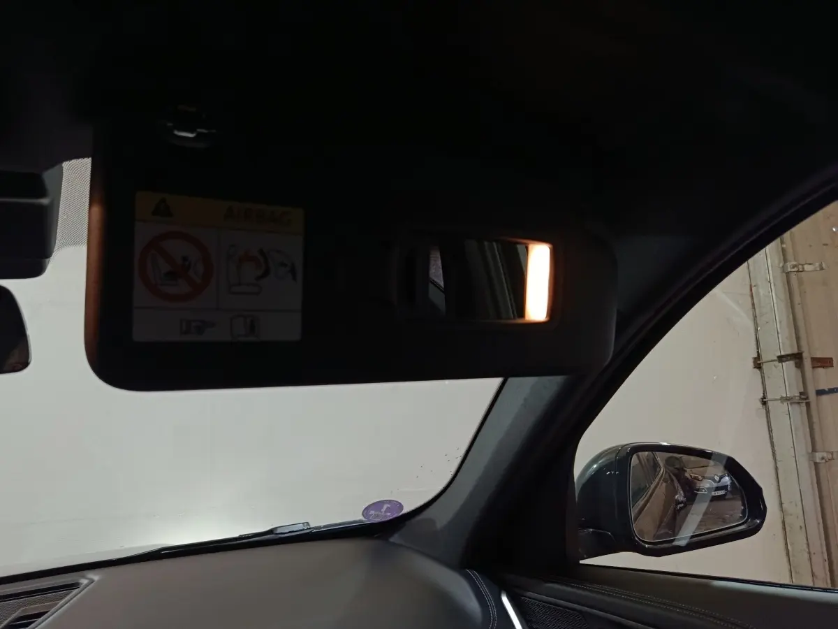 Intérieur BMW X1 noir 2023, vue côté droit sur pare-soleil avec miroir éclairé et rétroviseur extérieur.
