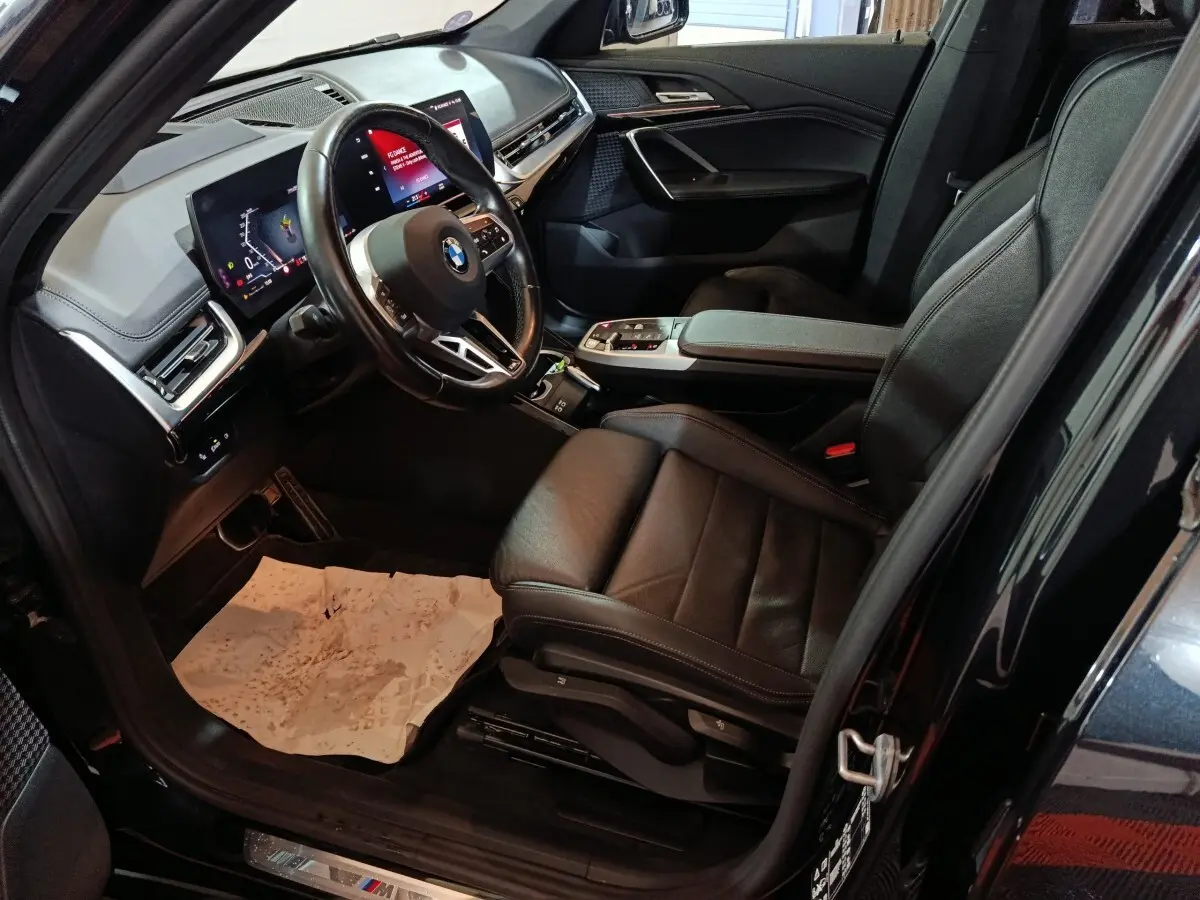Vue intérieure côté conducteur du BMW X1 xDrive23i M Sport 2023 noir, avec tableau de bord digital et sièges cuir noirs.