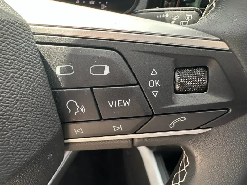 Gros plan sur les commandes multifonctions noires du volant cuir du SEAT Arona 2025, avec molette et boutons blancs.