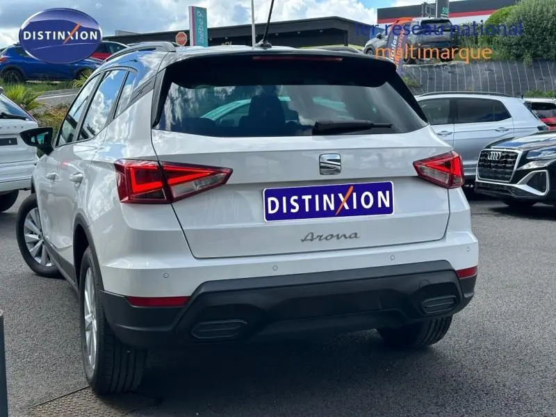 Vue 3/4 arrière d'un SEAT Arona blanc Nevada avec toit noir, feux arrière LED et double sortie d'échappement intégrée.